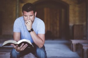 A closeup shot of a male sitting while reading the bible with a blurred background