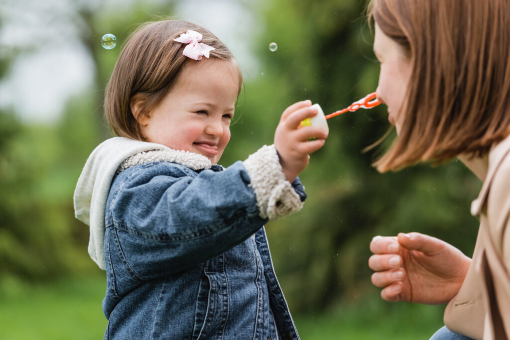 autistic child holding bubble wand near face of mother in park